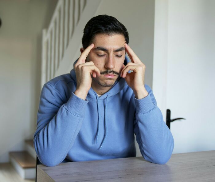 Man in blue hoodie sitting at table looking stressed, illustrating people dealing with partner shenanigans before leaving.