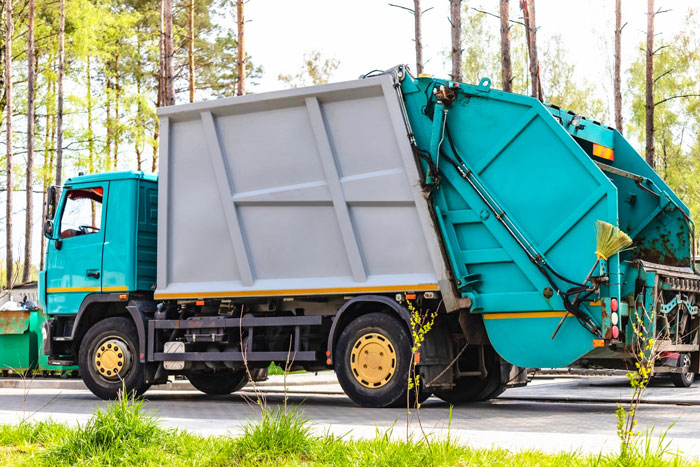 Garbage truck parked outdoors near trees and grass, representing California gull hitching an 80-mile ride. - 5