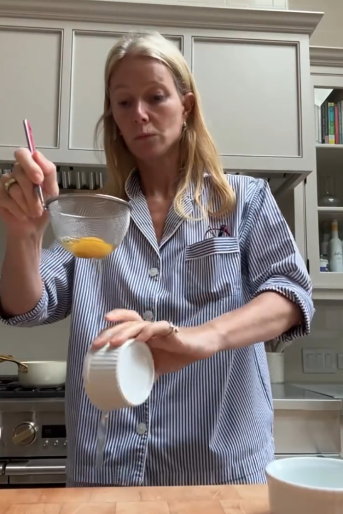 Gwyneth Paltrow in kitchen, pouring liquid while holding a strainer, showing trash-handling skills in cooking video. - 3