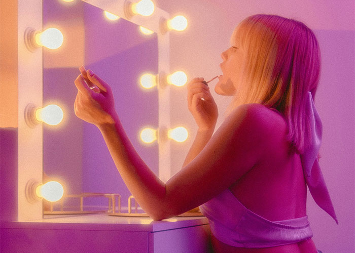 Young woman applying makeup in front of illuminated mirror, illustrating habits and decisions affecting life quality and regret.