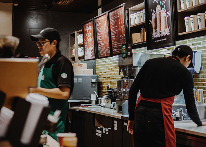 Two baristas working behind the counter in a coffee shop, showing daily habits that impact life quality.