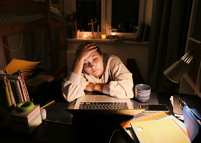Woman looking stressed and tired while working late on a laptop, showing habits that reduce life quality and cause regret.