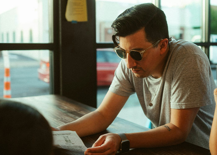 Man in sunglasses reading paper at table, reflecting on habits and decisions that reduce life quality and cause regret