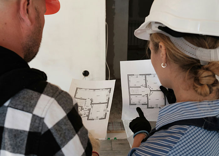 Two construction workers wearing helmets examining building plans discussing habits and decisions that reduce life quality.