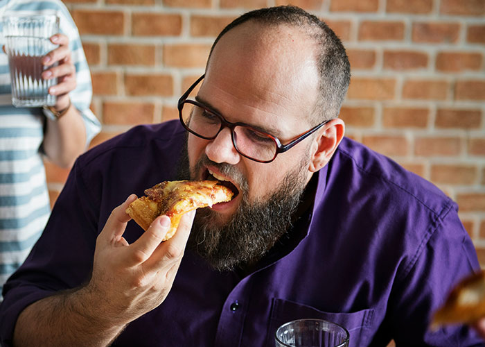 Man with glasses eating pizza indoors, illustrating habits and decisions that reduce life quality.