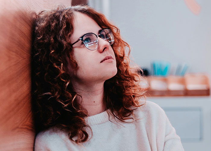 Young woman with curly hair and glasses looking thoughtful, symbolizing habits and decisions that reduce life quality.