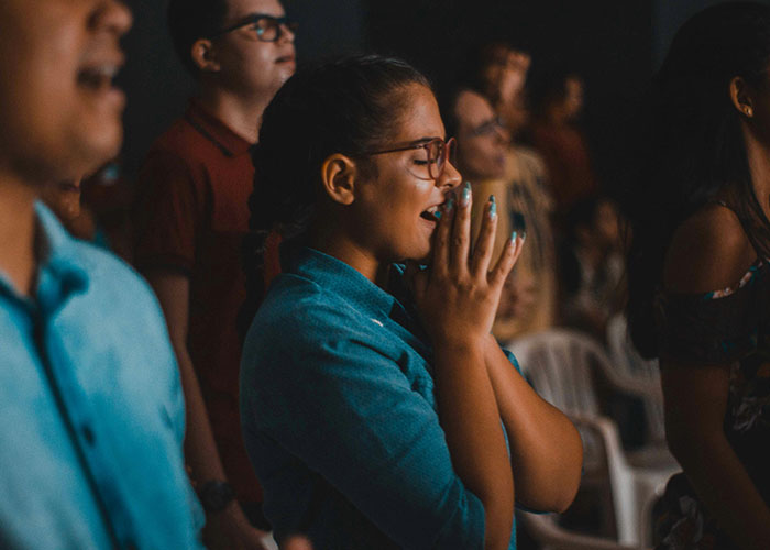 Young woman with glasses praying with hands clasped, illustrating habits and decisions that reduce life quality regret.