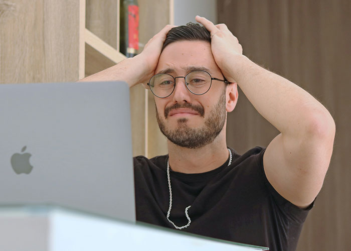 Man with glasses stressed and holding head while using laptop, illustrating habits and decisions that reduce life quality.