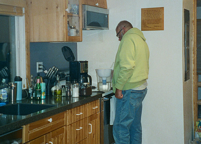 Middle-aged man in a kitchen wearing a green hoodie, reflecting on habits and decisions affecting life quality.