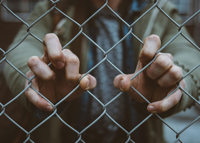 Hands gripping a chain-link fence symbolizing habits and decisions that regretfully reduce life quality and personal freedom.