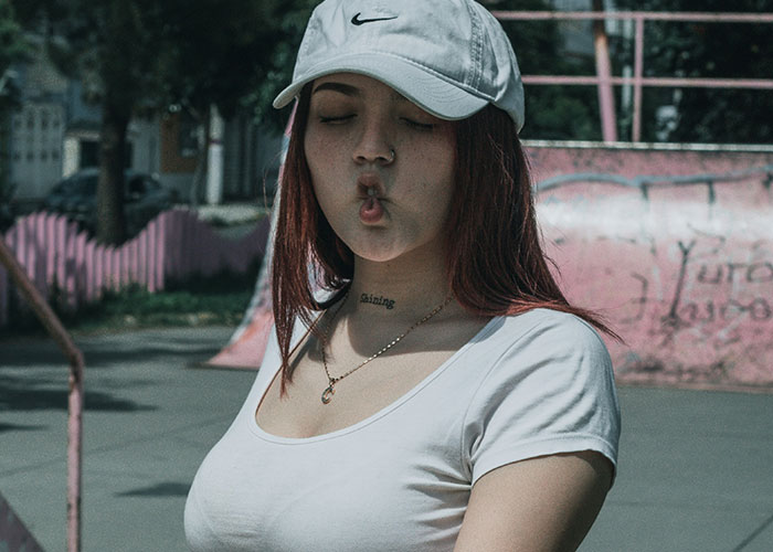 Young woman wearing a white shirt and cap making a playful face in an urban setting about habits and decisions regret.