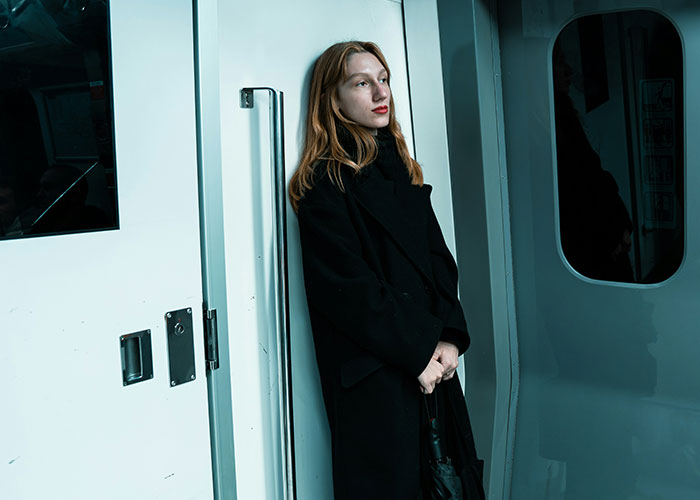 Young woman in a black coat standing alone on a subway train, reflecting on habits and decisions that reduce life quality.