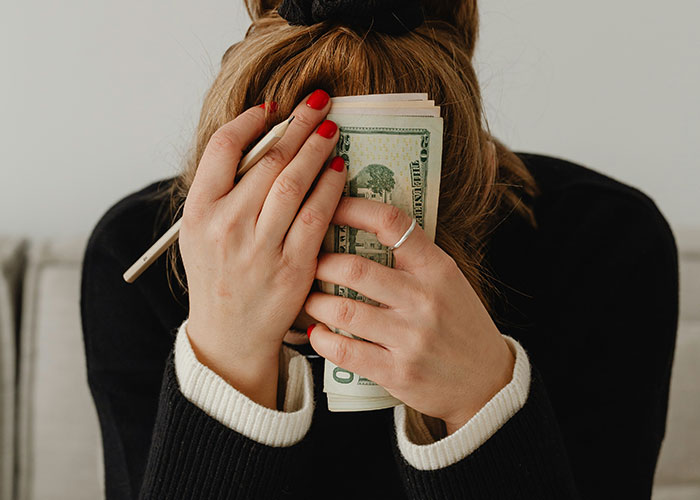 Person covering face with money and pen, illustrating habits and decisions that reduce life quality and cause regret.