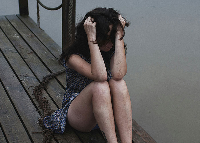 Woman sitting on a wooden dock holding her head, symbolizing regret and poor life quality habits and decisions.