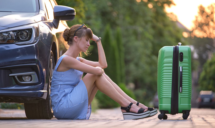 Woman sitting on sidewalk with green suitcase and car nearby, appearing upset while dealing with half-sister situation. Woman sitting on sidewalk with green suitcase and car nearby, appearing upset while dealing with half-sister situation.