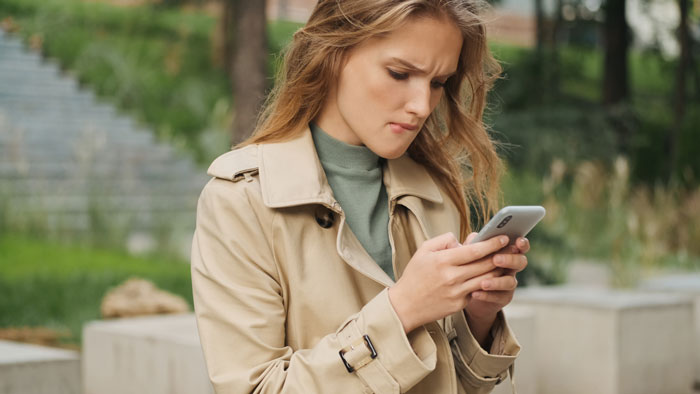 Woman in a beige coat looking upset at smartphone, reflecting tension with half-sister asking for help after 17 years. Woman in a beige coat looking upset at smartphone, reflecting tension with half-sister asking for help after 17 years.