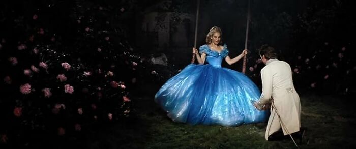A woman in a blue ball gown on a swing with a man in white kneeling nearby, illustrating worst movie tropes.