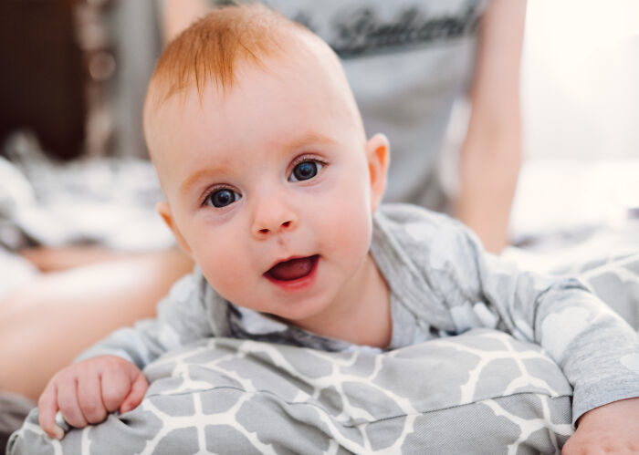 Close-up of a baby lying on a bed with a parent in the background, related to women sharing experiences after birth.
