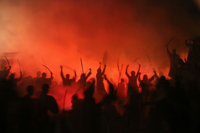 Silhouettes of people waving sticks amid red smoke, symbolizing warning and red flag behavior in crowds. - 12