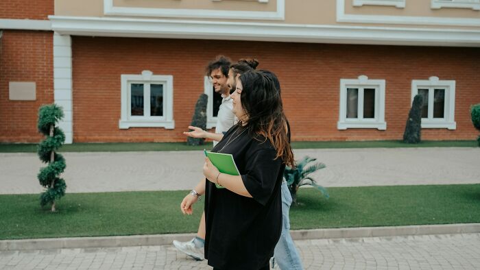 Three people walking outside a building, one holding a green notebook discussing unusual private investigator cases. - 31