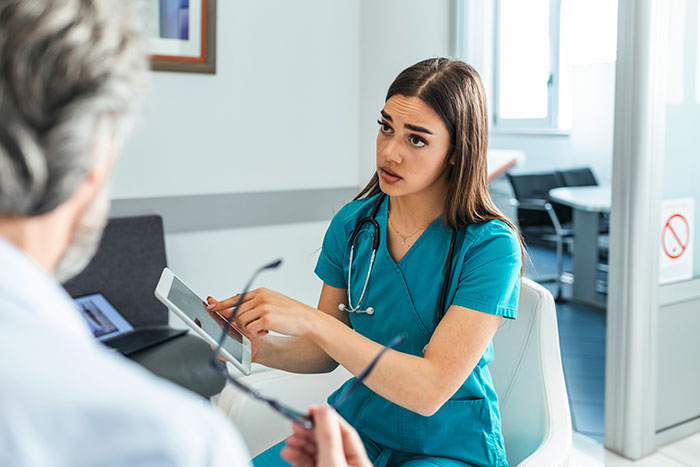 Hospital staff in blue scrubs discussing patient information on a tablet in a modern medical office.