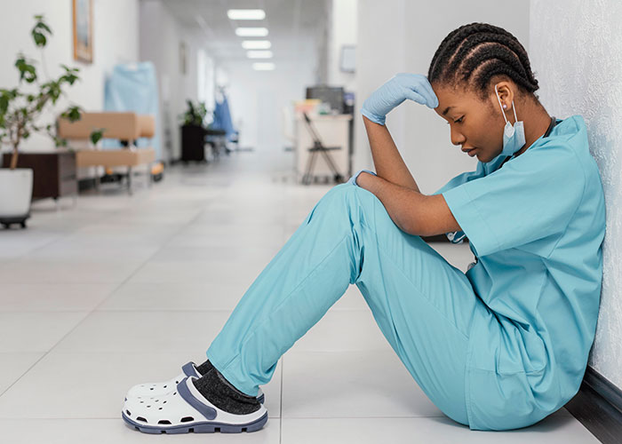 Hospital staff in scrubs sitting on floor of hospital corridor, appearing exhausted after witnessing wild common events.
