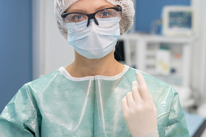 Hospital staff wearing surgical mask and gown preparing for procedure in a clinical setting with medical equipment background.