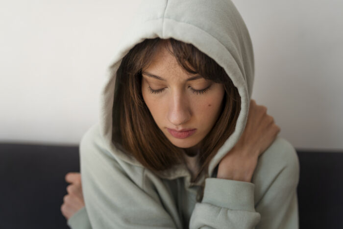 Young woman in a hoodie hugging herself with eyes closed, reflecting on toxic femininity behaviors and emotions. - 44