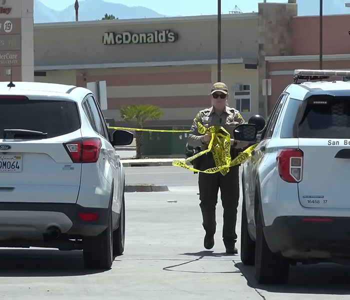 Police officer setting up crime scene tape outside convenience store near vehicles after horrifying teddy bear covered in apparent human remains found