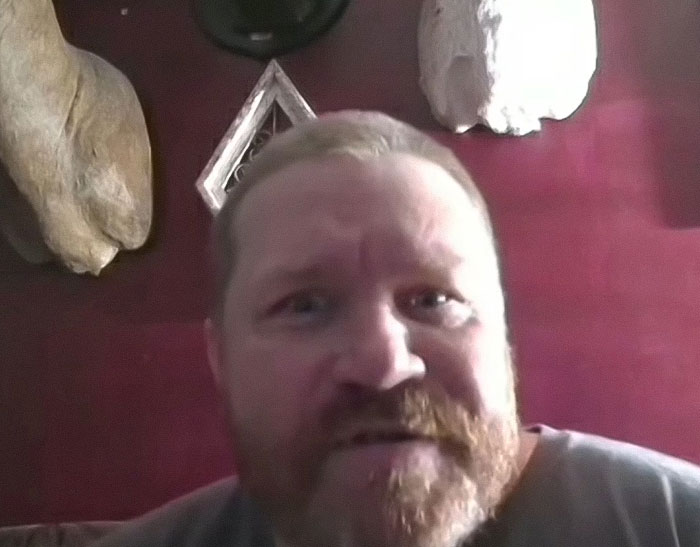 Man with red beard in a dim room, discussing a horrifying teddy bear covered in apparent human remains.
