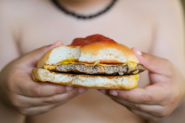 Person holding a half-eaten McDonald's cheeseburger, representing McDonald's employees sharing bizarre experiences.