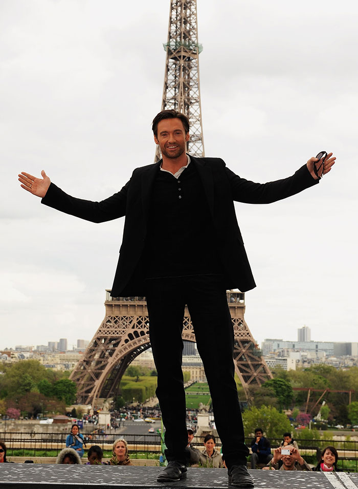 Tall star posing with arms outstretched in front of the Eiffel Tower, highlighting surprising super tall celebrity heights.