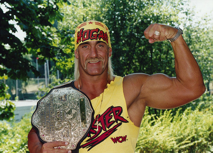 Wrestling star posing outdoors with championship belt and flexed arm, representing stars we've lost this year.