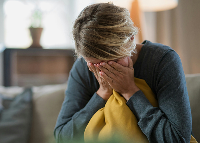 Sad mom sitting on couch covering her face, feeling overwhelmed as marriage falls apart due to husband&rsquo;s new hobby