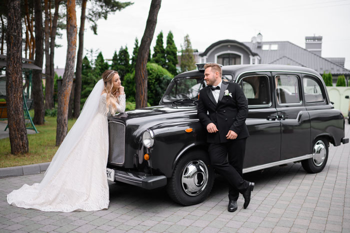 Bride and groom posing by vintage black car, highlighting car service business at wedding event outdoors. - 5