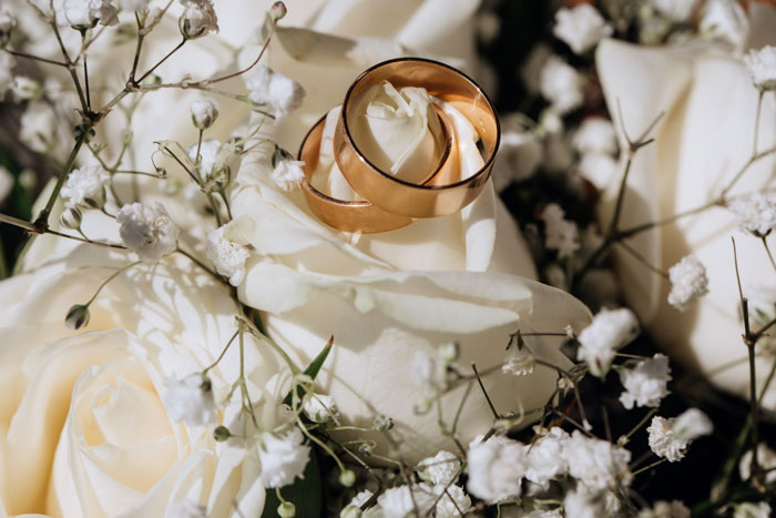Two gold wedding rings resting on a white rose surrounded by small white flowers for sister's car service business. - 1