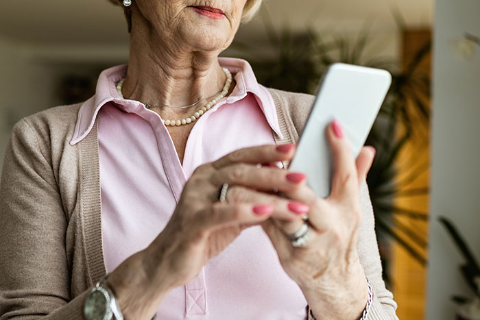 Older woman holding a smartphone, looking concerned while reading a message about husband texting his mother secretly.