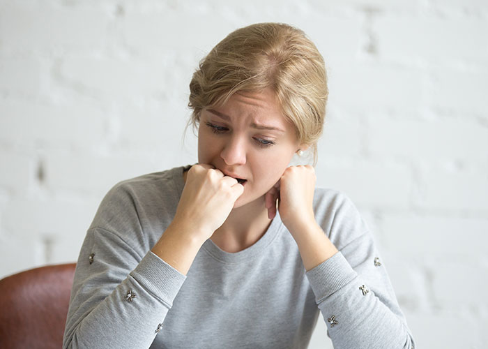 Worried woman biting her fist and looking down, portraying emotions related to manipulative husband and the internet. - 34