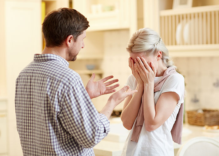 Woman covering face in distress while a man talks, depicting a manipulative relationship situation at home. - 1
