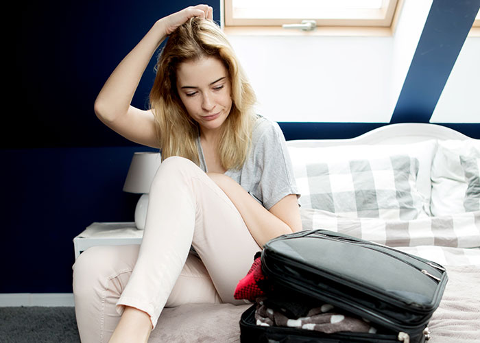 Woman sitting on bed looking thoughtful, packing suitcase, symbolizing woman leaving manipulative husband with help of internet. - 53