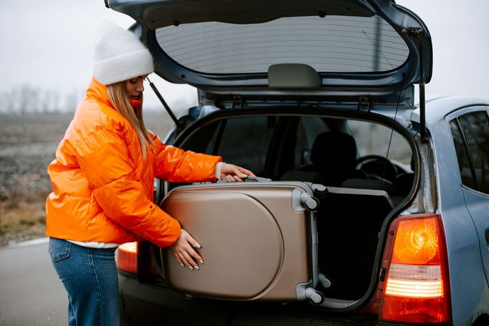 Woman packing suitcase into car trunk, illustrating travel difficulties linked to wife's weird quirk affecting trips. - 1