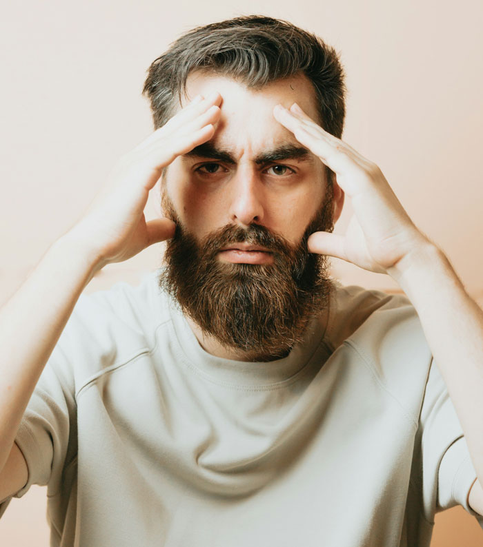 Stressed man with beard holding temples, reflecting on wife filing for divorce after strange traveling quirk revealed. - 5