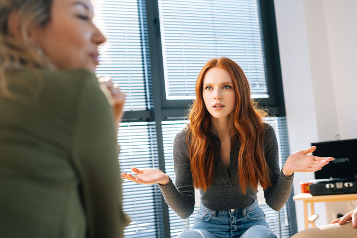 Young woman with red hair discussing with others, expressing frustration about parents wanting to wake man who sleeps past noon.