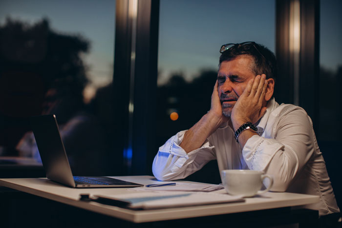 Man frustrated and tired at laptop late at night, reflecting stress from parents wanting to wake him despite pregnant wife.
