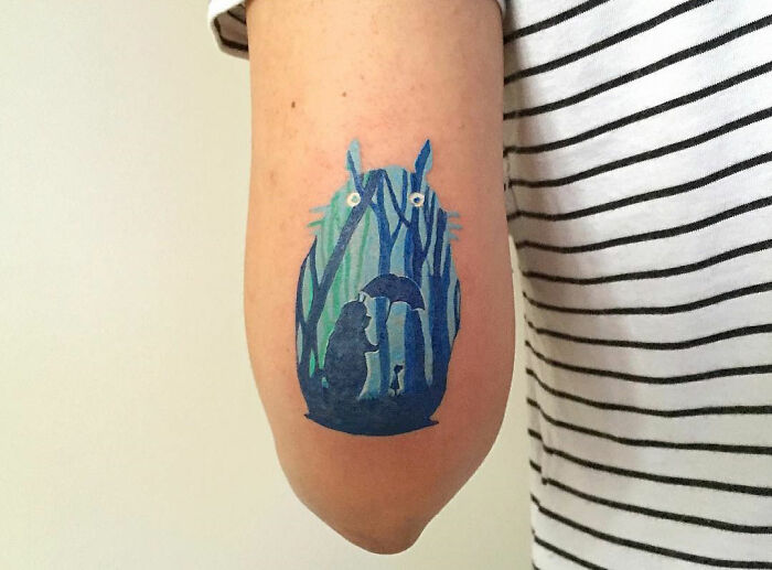 Tattoo of a blue forest creature holding an umbrella on a person's arm, showcasing one of the best tattoos designs.