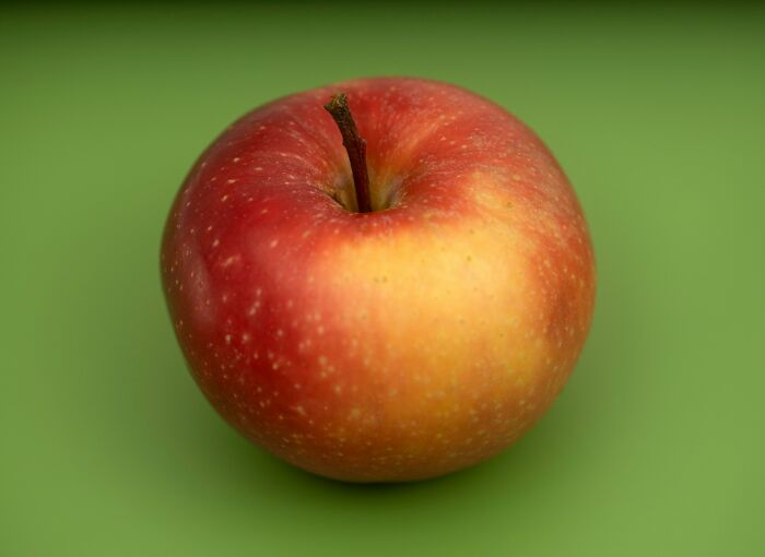 Red and yellow apple with a stem on a smooth green background representing imagine the smell concept.