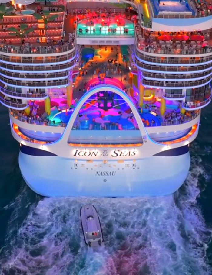 Passenger flips over infinity pool edge on a colorful cruise ship deck with lively crowd and a boat trailing behind. - 10
