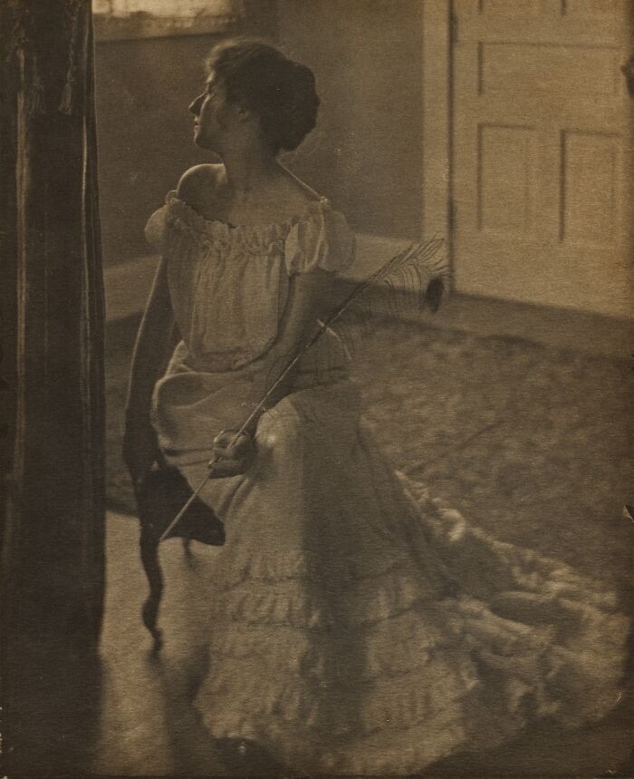 Vintage sepia photo of a woman in a 1900s dress holding a feather, showcasing beauty of women from the 1900s.