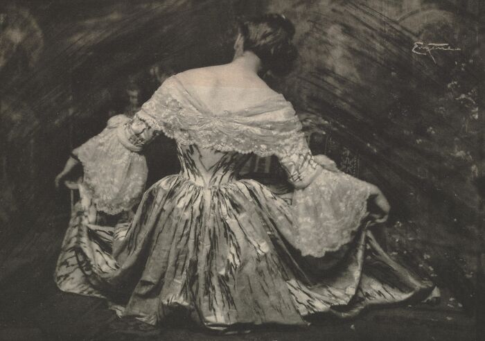 Woman in 1900s vintage dress with lace sleeves, seated and holding her skirt, showcasing beauty of women from the early 1900s.