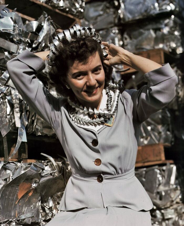 Woman at work during WWII smiling with curled metal strips around her head and neck in a factory setting.